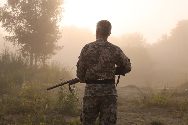 Man with hunting rifle wearing camouflage outdoors, back view