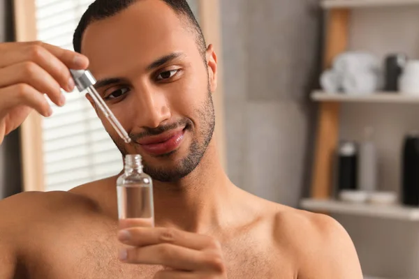 Handsome man with cosmetic serum in hands in bathroom