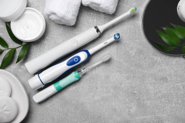 Elektrikli diş fırçaları, sarılı havlu ve yapraklar gri desenli masa, düz yatak. Metin için boşluk