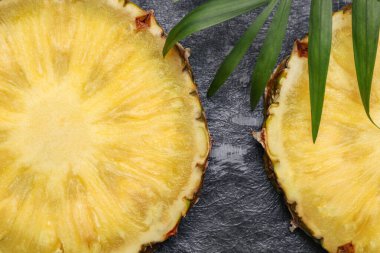 Lezzetli olgun ananas dilimleri ve siyah desenli masa üzerinde yeşil yapraklar, yakın plan.