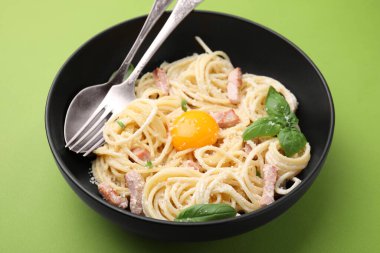 Yumurta sarısı ve açık yeşil arka planda çatal bıçaklı Carbonara makarnası. Yakın plan.