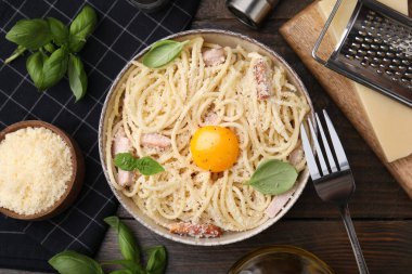 Bir kase lezzetli Carbonara makarnası fesleğen yaprakları ve yumurta sarısı ile ahşap masa, düz yatıyordu.