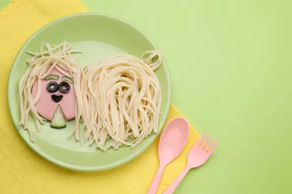 Creative serving for kids. Plate with cute dog made of tasty pasta, sausage and cucumber on green table, flat lay. Space for text
