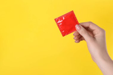 Sarı arka planda prezervatif tutan kadın, yakın plan. Metin için boşluk