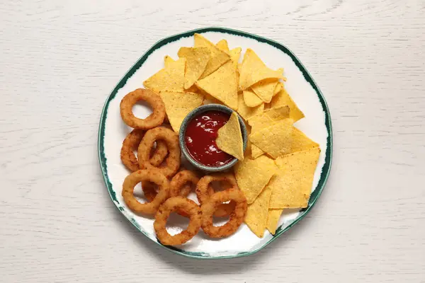 Tasty tortilla and fried onion rings with ketchup on white wooden table, top view
