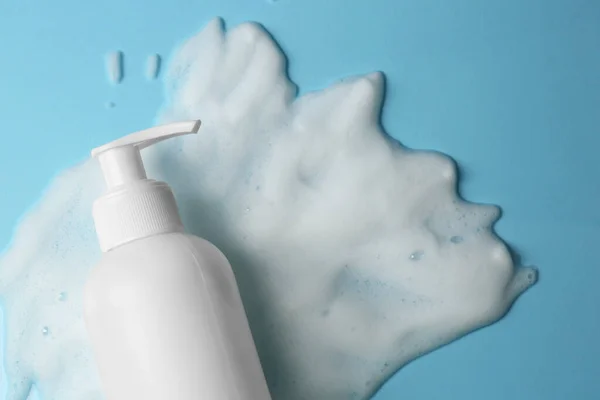 Bottle of face cleanser and white foam on light blue background, top view with space for text. Skin care cosmetic