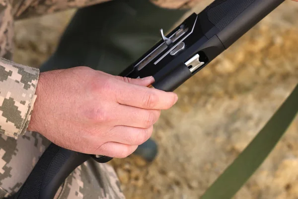 Man wearing camouflage with hunting rifle outdoors, closeup