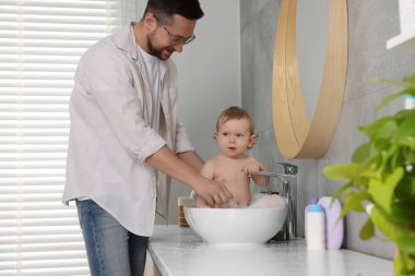 Babası küçük bebeğini evde lavaboda yıkıyor.