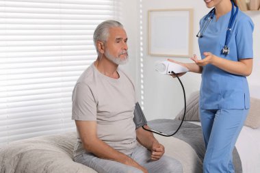 Genç bir sağlık çalışanı, yaşlı adamın içeride kan basıncını ölçüyor.