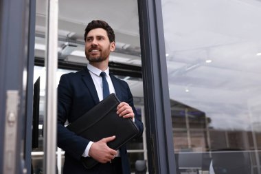 Ofis dışında deri portföyü olan erkek emlakçı.