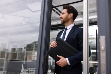 Ofis dışında deri portföyü olan erkek emlakçı.