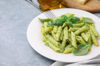 Pesto soslu lezzetli makarna ve açık gri masada fesleğen, yakın plan. Metin için boşluk