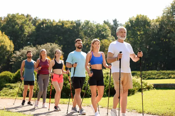 Güneşli bir günde bir grup insan parkta sırıkla yürüyor.