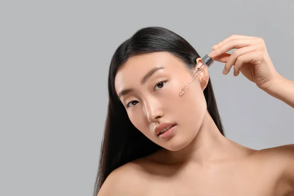 Wanita Muda Cantik Mengaplikasikan Serum Kosmetik Wajahnya Pada Latar Belakang — Stok Foto