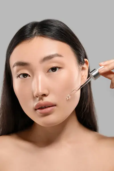 Wanita Muda Cantik Mengoleskan Serum Kosmetik Wajahnya Latar Belakang Abu — Stok Foto