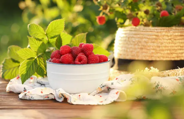 Tasty Ripe Raspberries Bowl Green Leaves Straw Hat Wooden Table — Stock Photo, Image
