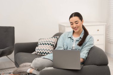 Evdeki koltukta dizüstü bilgisayar kullanan kadın.