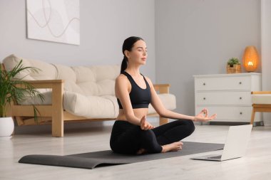 Evde yoga minderinde Padmasana çalışırken pratik yapan güzel bir genç kadın. Lotus pozu
