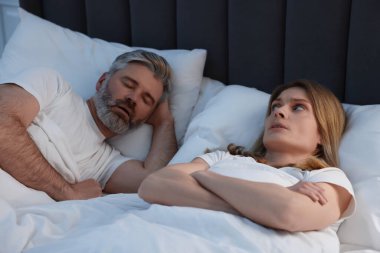 Evde yatakta horlayan kocasının yanında yatan sinirli kadın.