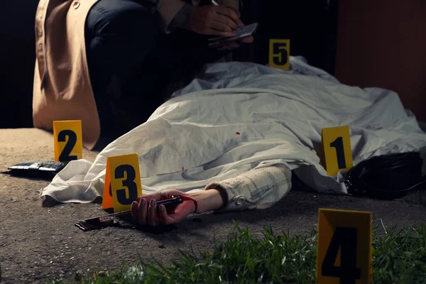 Investigator examining crime scene with dead body outdoors, closeup