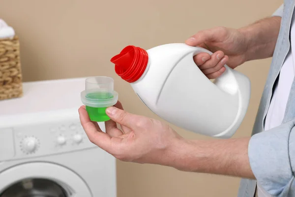 stock image Man pouring fabric softener from bottle into cap near washing machine indoors, closeup