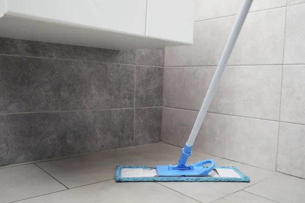 Cleaning grey tiled floor with mop indoors