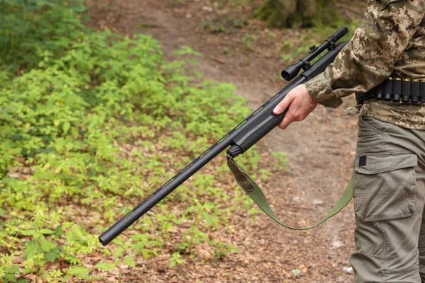 Man with hunting rifle wearing camouflage in forest, closeup