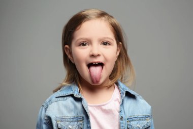 Emotional little girl showing her tongue on grey background clipart