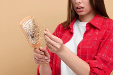 Kadın saçlarını bej arka planda fırçayla çözüyor, yakın plan. Alopecia sorunu