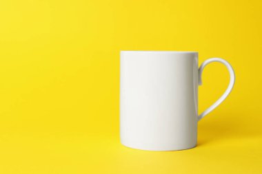 Sarı arka planda beyaz bir seramik bardak. Metin için boşluk