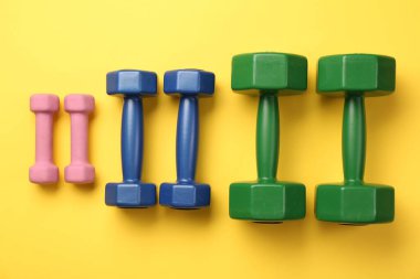 Different dumbbells on yellow background, flat lay clipart