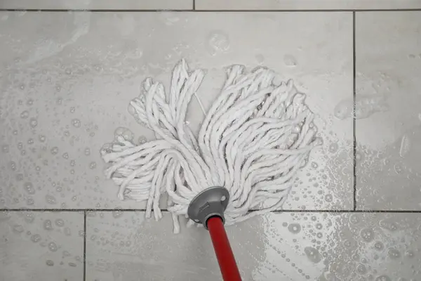 Cleaning grey tiled floor with string mop, top view