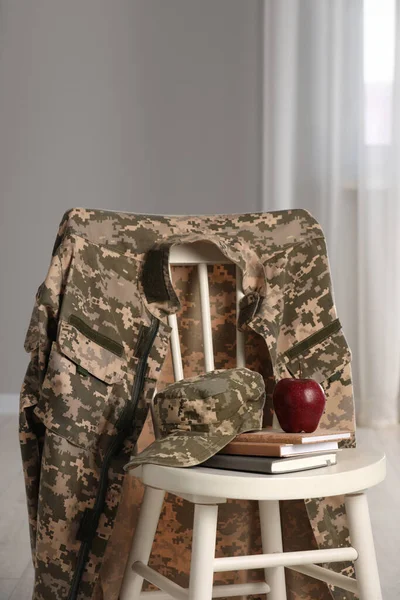 Chair with soldier uniform, notebooks and apple indoors. Military education