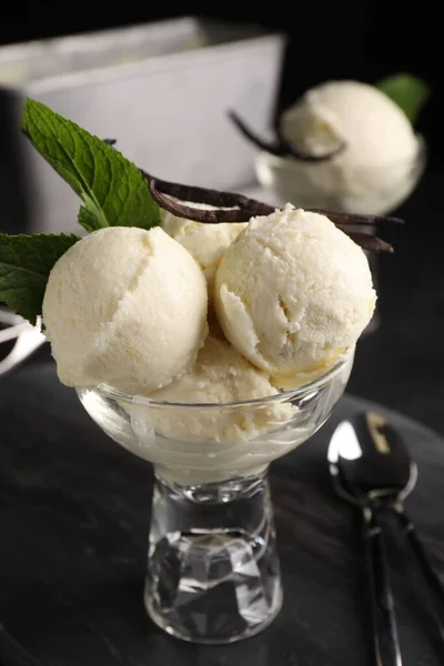 Tasty ice cream with vanilla pods and mint in glass dessert bowl on dark grey table, closeup