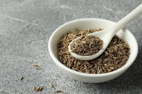 stock image Bowl of caraway (Persian cumin) seeds and spoon on gray textured table, closeup. Space for text