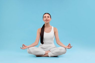 Açık mavi arka planda yoga yapan güzel bir genç kadın. Lotus pozu