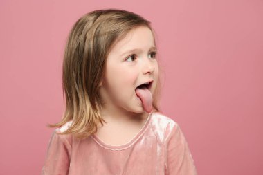 Dilini pembe arka planda gösteren komik küçük kız.