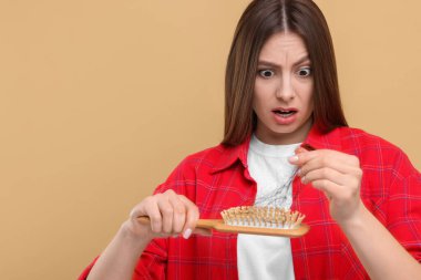 Duygusal kadın saçlarını bej arka plandaki fırçadan çözüyor, mesaj için yer açıyor. Alopecia sorunu