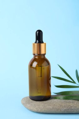 Açık mavi arka planda kozmetik yağı, taş ve yeşil yaprak ile şişe