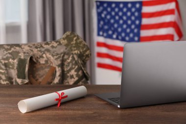 Laptop ve diploma, kapalı alanda ABD bayrağının yanındaki ahşap masada. Askeri eğitim