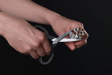 Sigara içmeyi bırak. Siyah arka planda sigara kesen kadın, yakın plan.