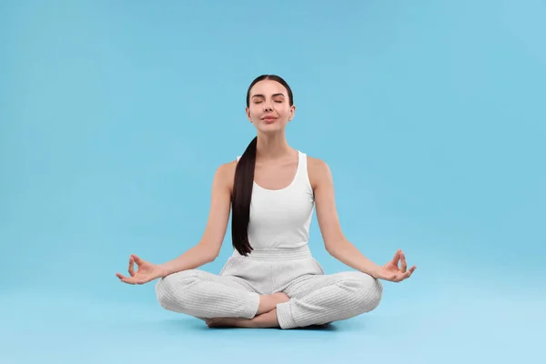 Beautiful young woman practicing yoga on light blue background. Lotus pose