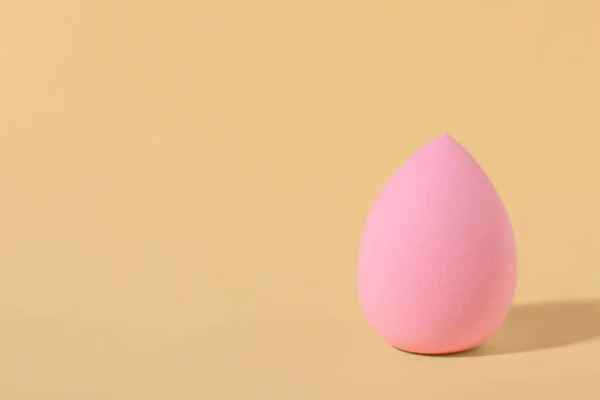 Pink makeup sponge on beige background, space for text