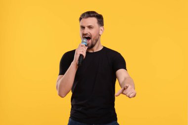 Sarı arka planda mikrofonlu yakışıklı bir adam şarkı söylüyor.