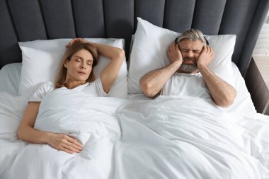Evde yatakta horlayan karısının yanında kulaklıkları olan sinirli bir adam.