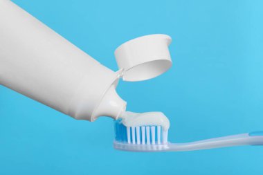 Açık mavi arkaplanda diş fırçasına yapıştırıcı uygulanıyor, yakın plan