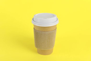 Sarı arka planda plastik kapaklı kağıt bardak. Kahve hazır.