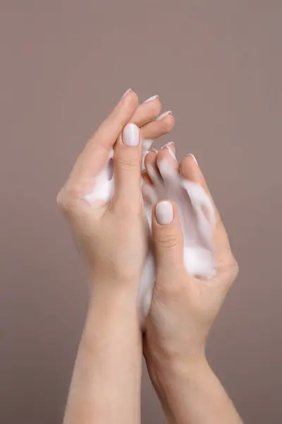 Woman washing hands with cleansing foam on brown background, closeup. Skin care cosmetic