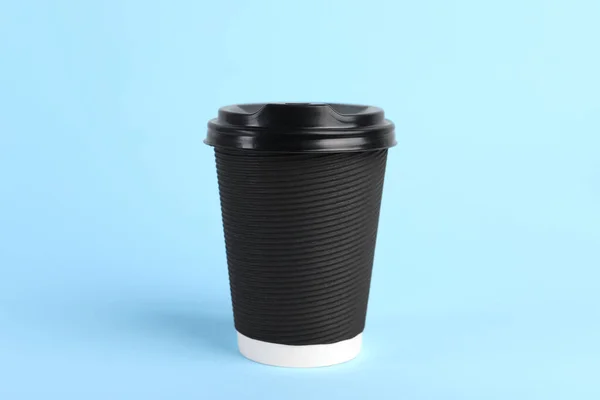 Black paper cup with plastic lid on light blue background. Coffee to go