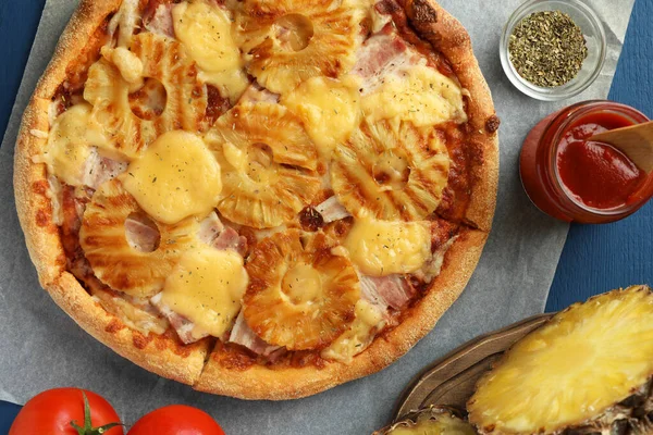 Delicious pineapple pizza and ingredients on blue table, flat lay